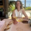 Doula agency owner smiling at an outdoor restaurant table in Spain with wine and dessert, enjoying a worry-free family vacation.